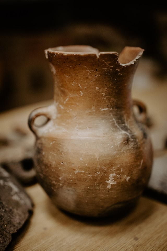 An ancient, cracked earthenware jar sitting in soft lighting, showcasing its fragile textures