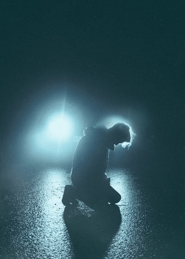 A man kneeling in prayer in dark shadows