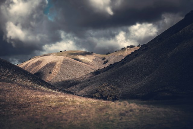 A rugged, barren Judean hillside under dramatic storm clouds